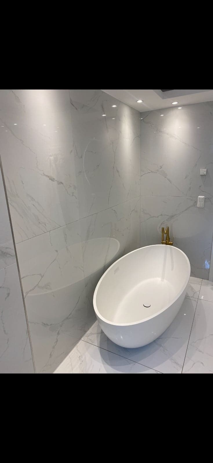 Freistehende Naturstein-Badewanne vor großformatigen Marmorfliesen