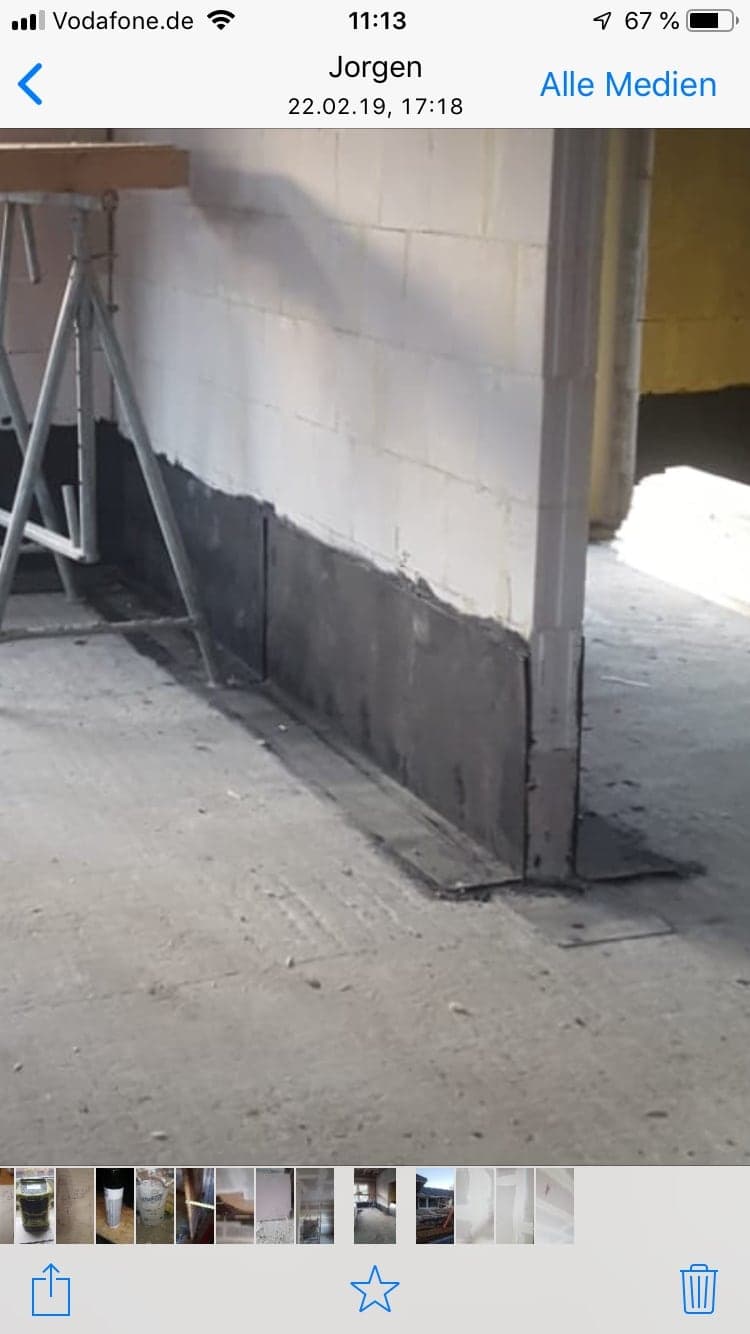 Schwarze Bitumen-Abdichtung am Sockel einer Kellerwand