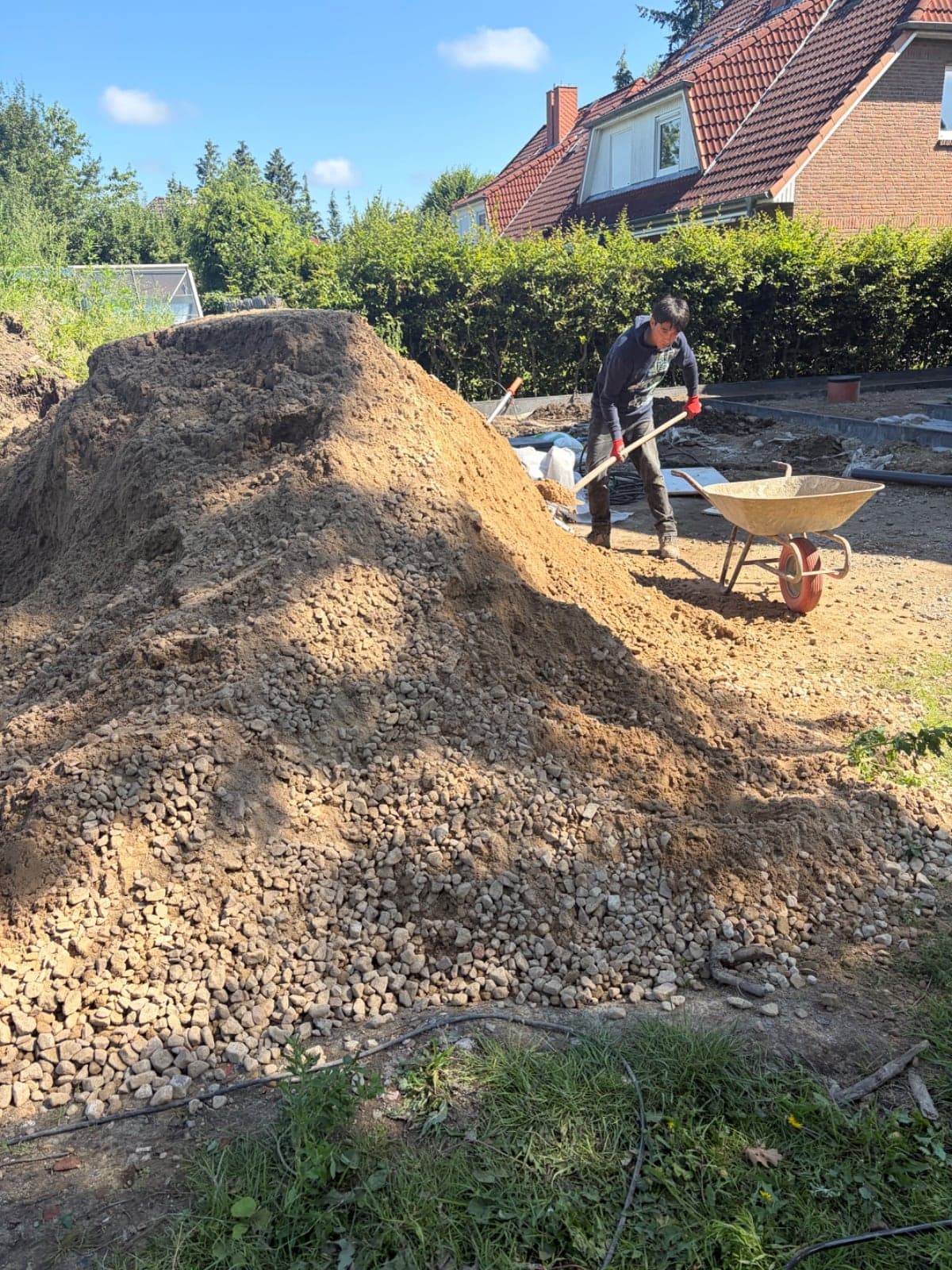 Mitarbeiter beim Verteilen von Schotter mit Schaufel und Schubkarre